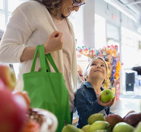 A little girl holding an apple, looking up at her mother in a grocery store.