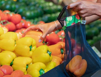 Une personne met des poivrons orange dans un sac réutilisable à l’épicerie.
