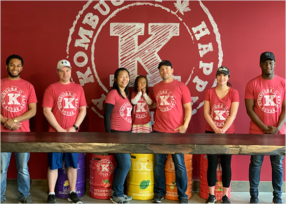 Happy Belly Kombucha employees standing behind a table wearing red shirts.