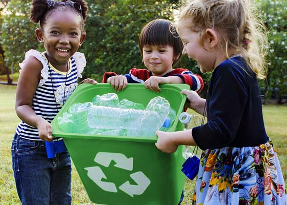 Trois enfants tiennent un bac de recyclage rempli de bouteilles de plastique.