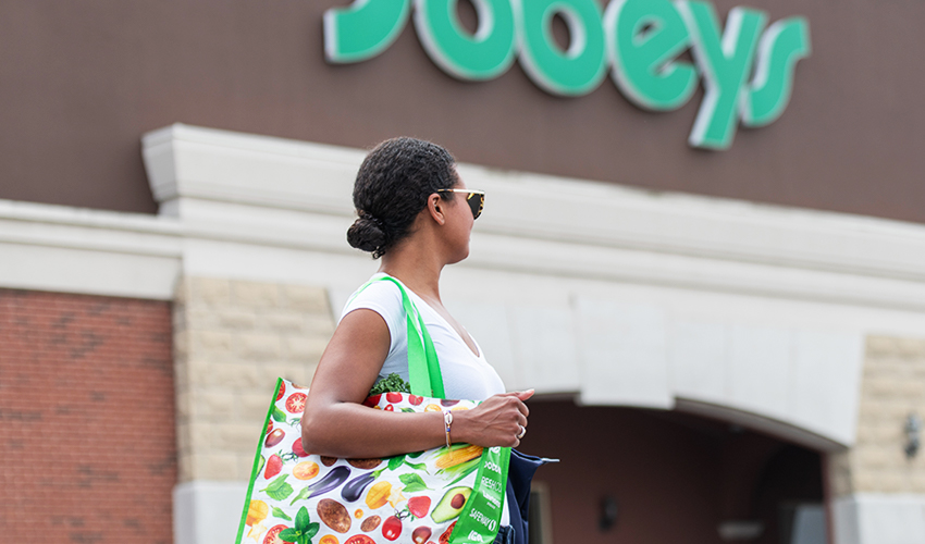 Woman holding reusable shopping bag standing outside of a Sobeys store.