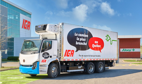 Electric delivery truck parked outside an IGA store and a Sobeys store.