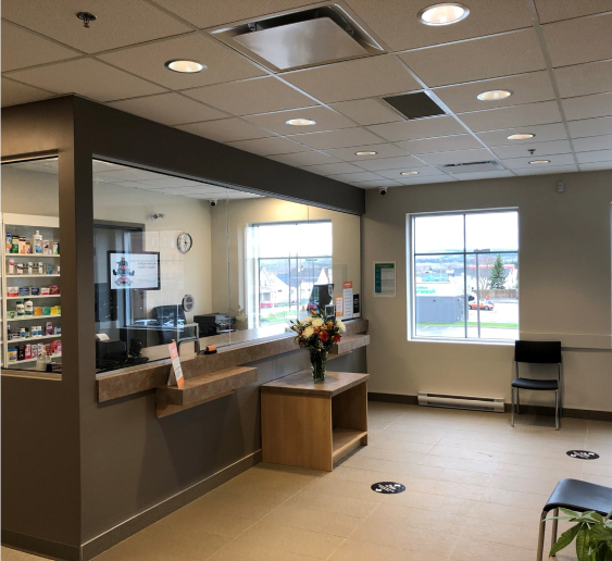 An image of a well-lit reception area with a counter, plexiglass barrier, floral arrangement, and seating.