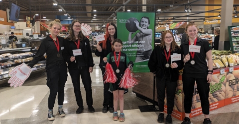 A group of six people, predominantly female, stand in a grocery store holding informational flyers.