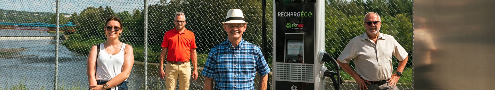 In this image, some people are standing in front of the IGA Ev charger and getting their picture taken.