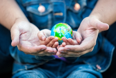 Two pairs of hands, one adult and one child, hold a small globe together, symbolizing unity and shared responsibility for the Earth.