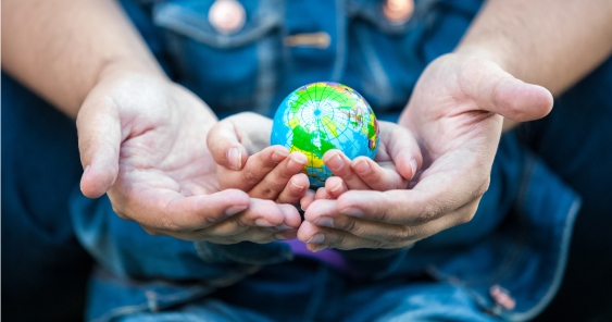 Two pairs of hands, one adult and one child, hold a small globe together, symbolizing unity and shared responsibility for the Earth.